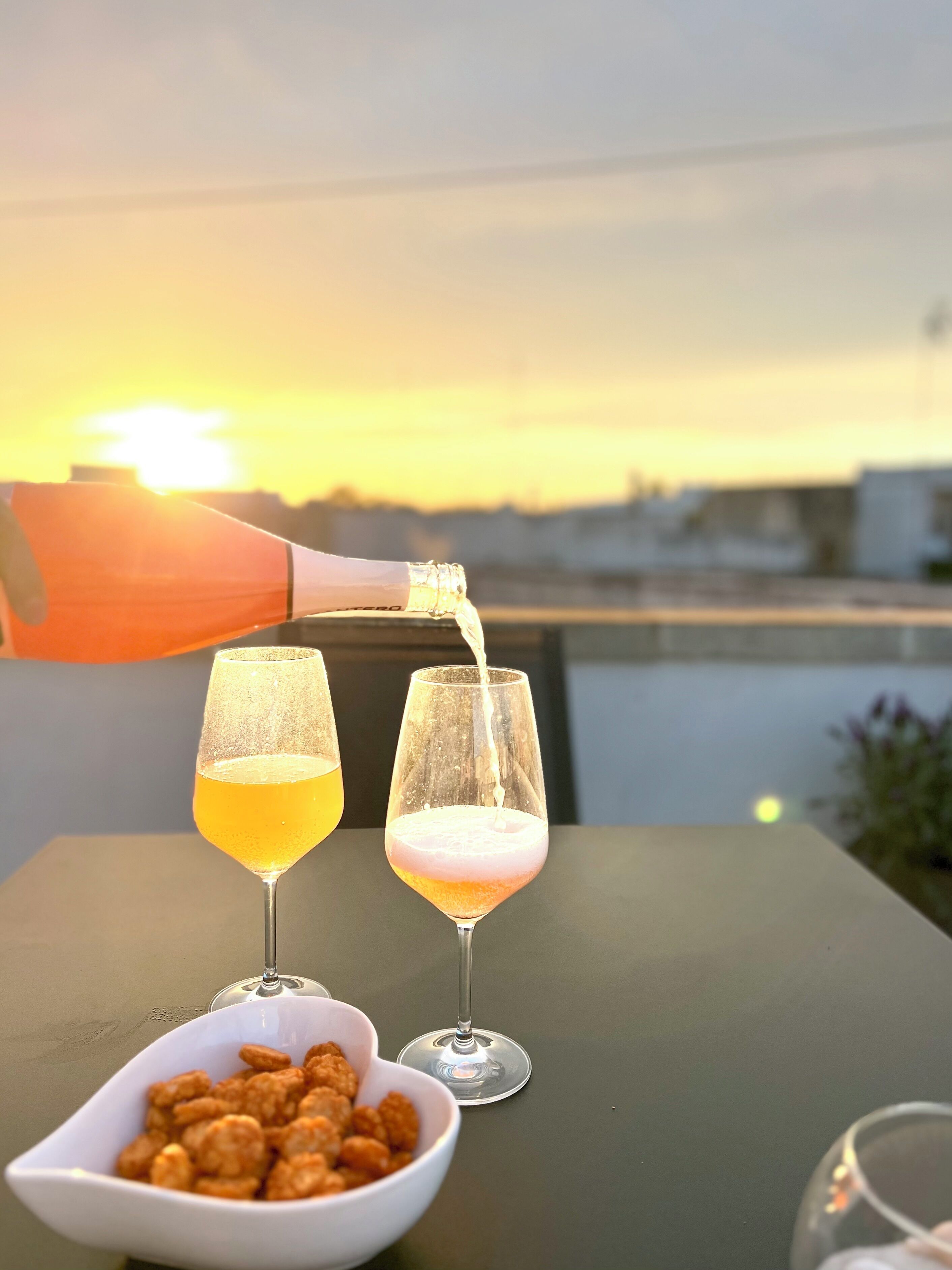 Two glasses of a yellowish beverage on a table with a sunset in the background.