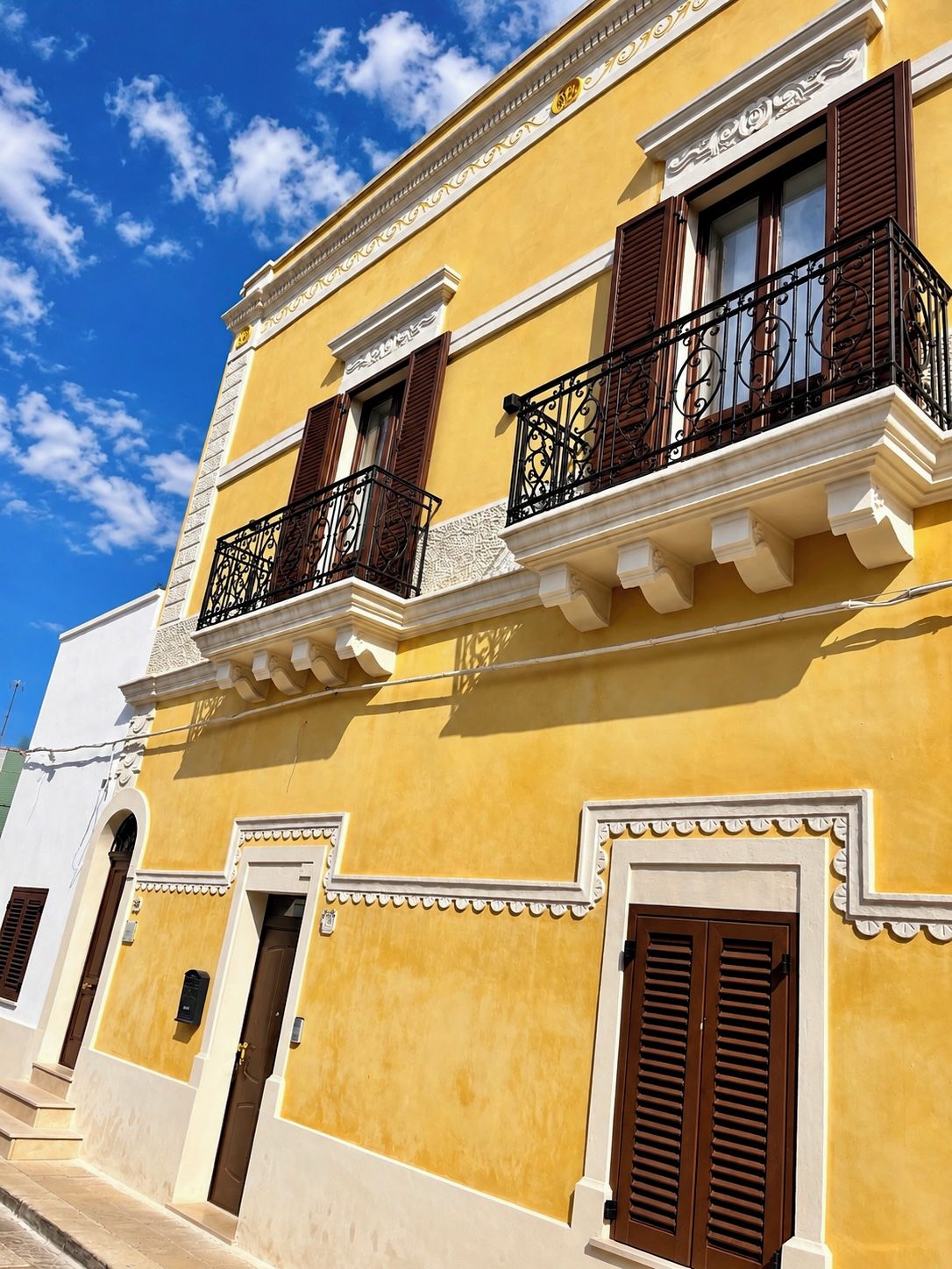 A yellow building with balconies, a white door, and a window with shutters.