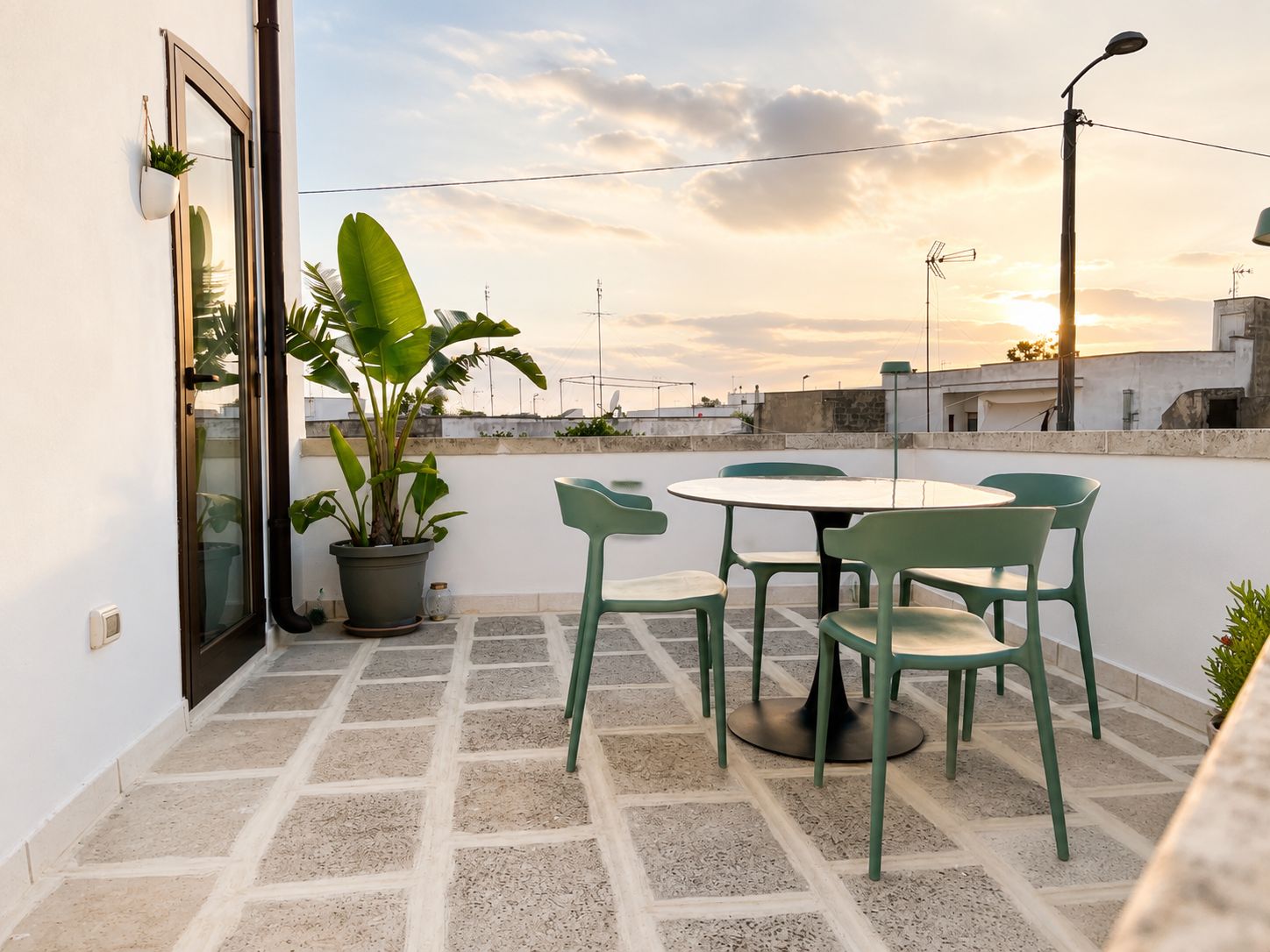 Une terrasse sur le toit, avec une table ronde et des chaises, des plantes en pot et une vue sur le coucher de soleil.
