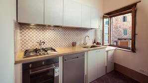A compact kitchen with a gas stove, dishwasher, and a window overlooking a stone building. - Villa Delizia, ArcenoRentalsClub, house in Chianti with garden, Concierge, Wifi (Villa A Sesta)
