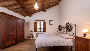 A bedroom with a wooden bed, a nightstand, a wardrobe, and a window with a view of a building outside. - Villa Delizia, ArcenoRentalsClub, house in Chianti with garden, Concierge, Wifi (Villa A Sesta)