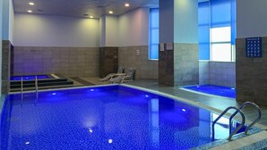 Una piscina con iluminación azul, tragaluz y toldo.