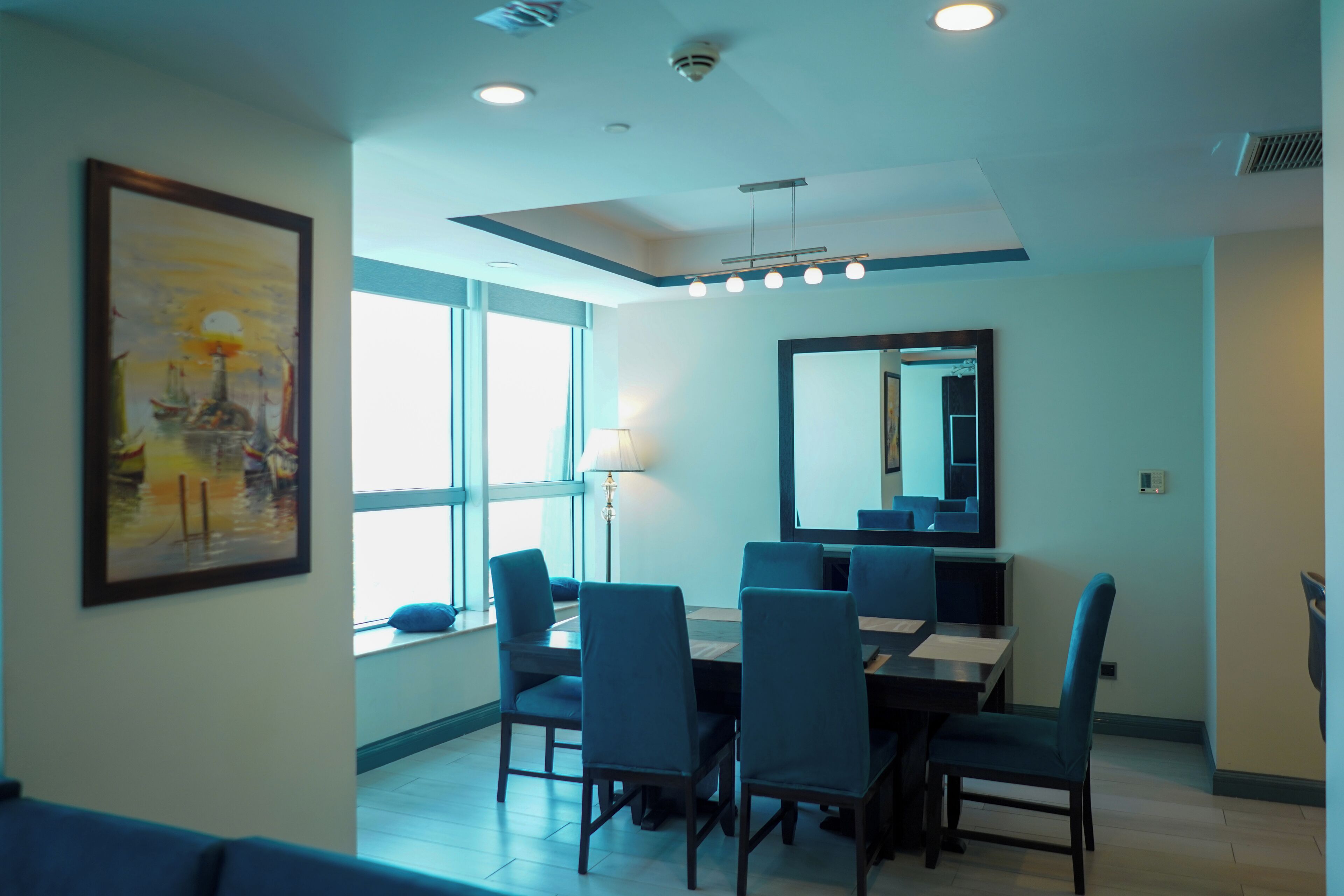 A dining area with a table, chairs, a lamp, and a large mirror on the wall.