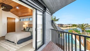 Une chambre à coucher avec un lit, une table de chevet et une lampe. Il y a un balcon qui offre une vue sur une piscine et d’autres bâtiments.