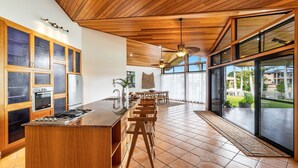 Une cuisine moderne dotée d’un îlot central, de meubles en bois et d’une grande porte-fenêtre coulissante donnant sur un patio.