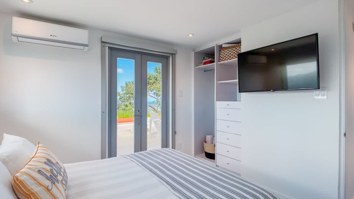 A bedroom with a bed, a TV mounted on the wall, a wardrobe, and a sliding glass door leading to an outdoor area.