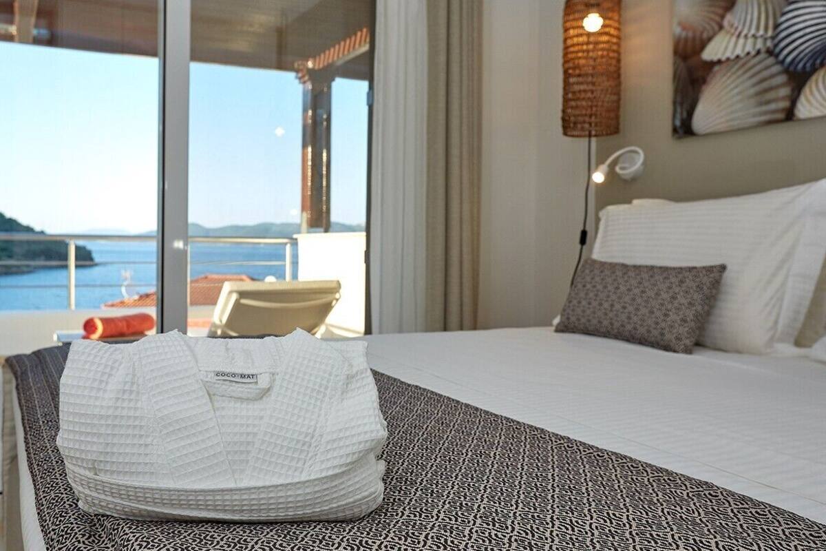 Une chambre d’hôtel avec un lit, une vue sur la mer et un balcon équipé d’une chaise.