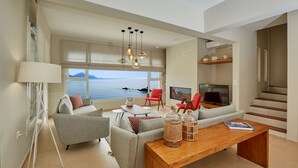 A modern living room with a large window offering a sea view, a wooden coffee table, and a TV.