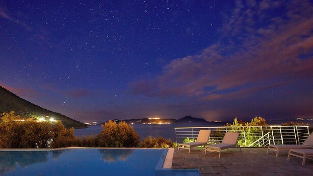 A swimming pool with lounge chairs and a night sky view.