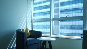 A room with a blue armchair, a small white table, and a large window with blinds. - The Haven Residence (Islamabad)