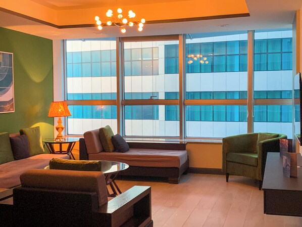 Una habitación de hotel moderna con un ventanal grande, un sofá, una mesita y una lámpara.