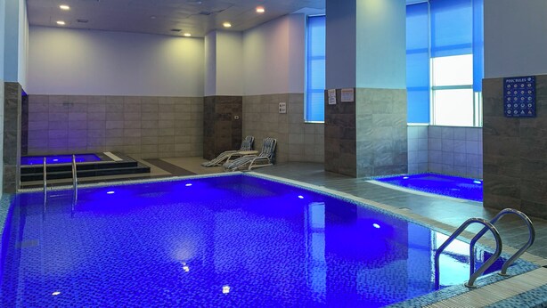 A swimming pool with blue lighting, tiled walls, and a poolside area with lounge chairs.