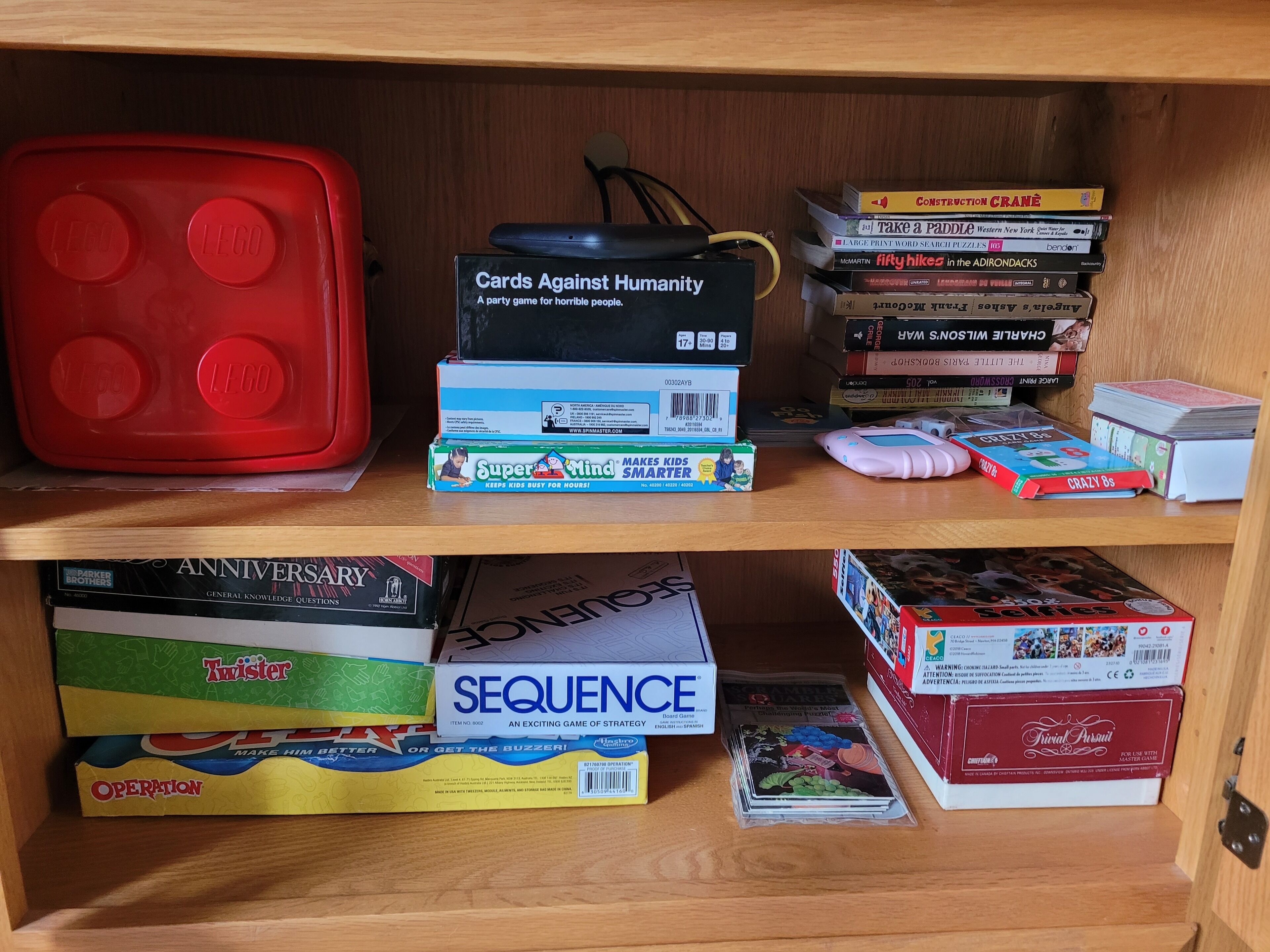 A shelf with various board games and books, including 'Cards Against Humanity' and 'Sequence'.