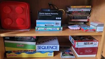 A shelf with various board games and books, including 'Cards Against Humanity' and 'Sequence'.