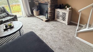 Un salon doté d’une cheminée en pierre, d’un téléviseur fixé au-dessus, d’un canapé, d’une table basse ronde et offrant une vue sur l’extérieur grâce à une grande fenêtre.