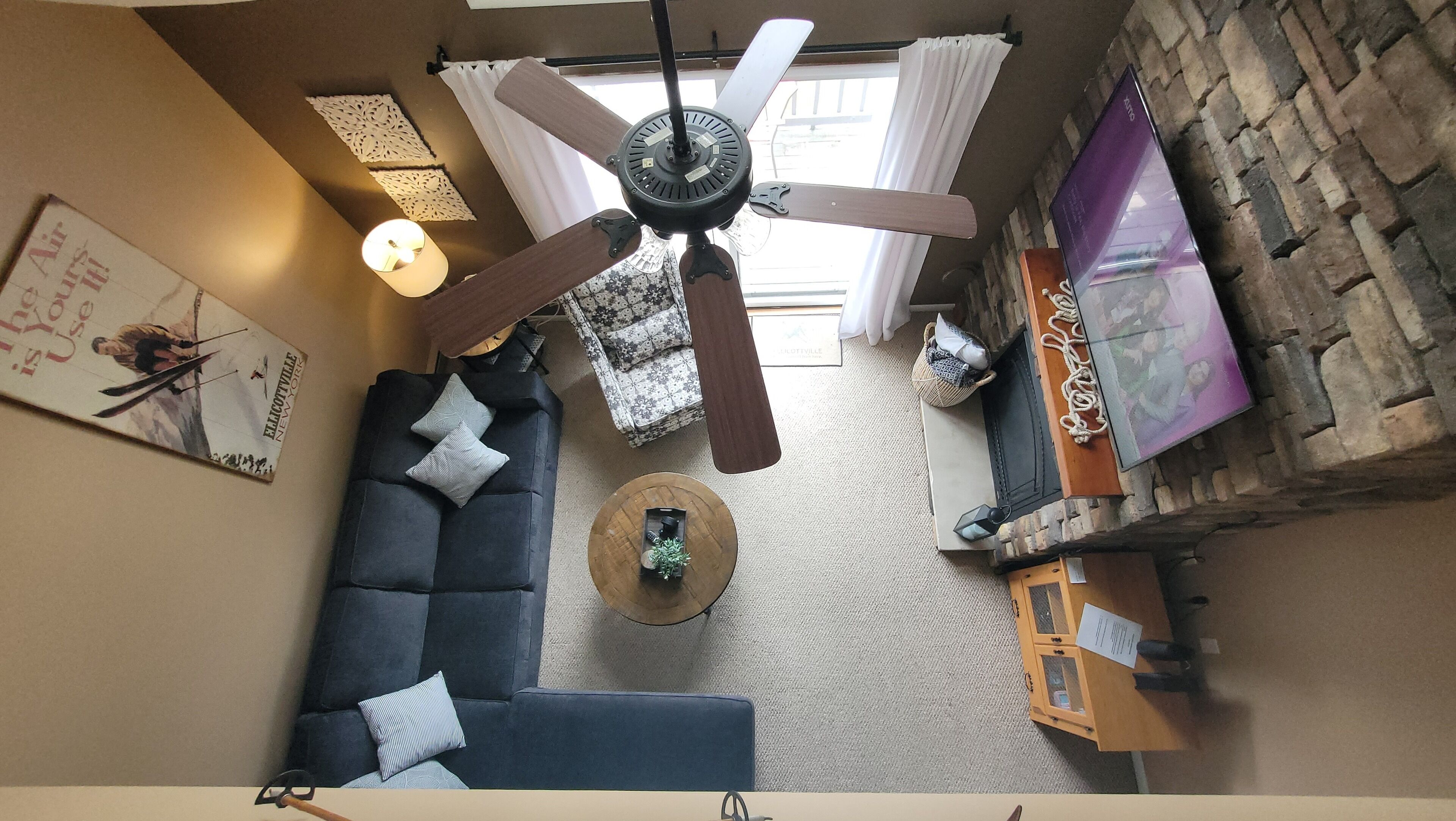 A living room with a ceiling fan, a sofa, a coffee table, a TV, and a stone wall.