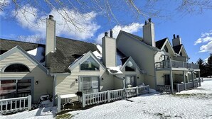 Une grande maison à plusieurs étages, avec une pelouse recouverte de neige et une clôture blanche.