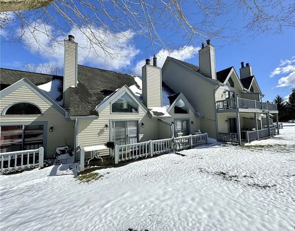 A large, multi-story house with a snow-covered lawn and a white fence.