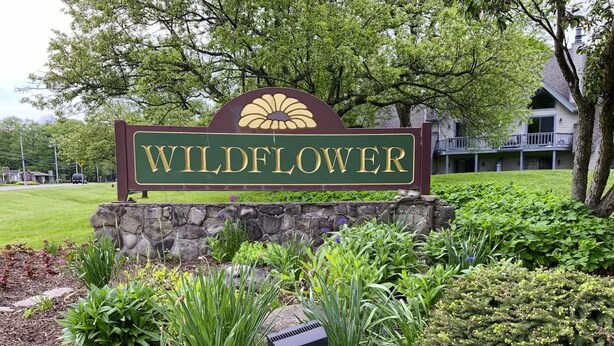 Une enseigne pour l’hôtel Wildflower Inn, avec un mur en pierre et un jardin aménagé.