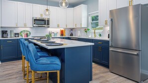 Una cocina moderna con armarios blancos, un refrigerador de acero inoxidable y taburetes de bar azules.