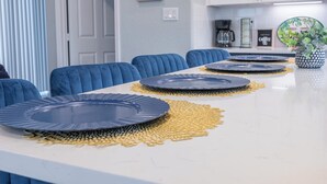 Un comedor con una mesa blanca, sillas azules y protectores de mesa decorativos.
