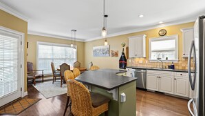 A kitchen with a central island, white cabinets, and a dining area with wicker chairs. - Lakefront Paradise with Spectacular Views! (Lexington)