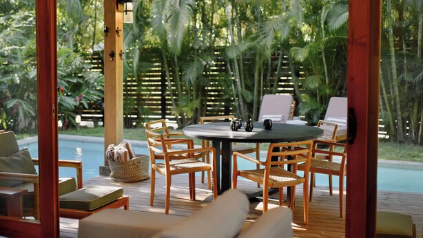 A wooden deck with a round table and chairs, a pool, and lush tropical vegetation in the background. - Chic surf and yoga villa 2-minute walk to beach (Guanacaste Province)