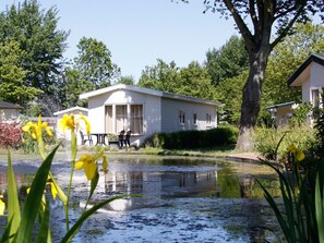 Ein weißer Wohnwagen mit einer kleinen Terrasse und einem Teich davor.