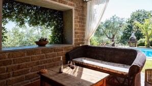 Un espace extérieur accueillant avec un canapé en osier et une table en bois, un mur en briques et une vue sur une piscine et des arbres.