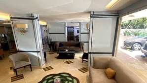 A modern living room with a beige sofa, a glass coffee table, and a dining area with a table and chairs. - Dreams Suites (Beirut)