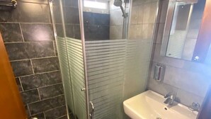 A modern bathroom with a glass-enclosed shower, a white sink, and dark tiled flooring. - Dreams Suites (Beirut)