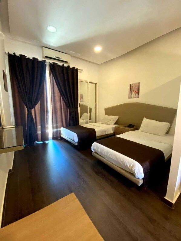 A hotel room with two beds, a wooden floor, a mirror, and a painting on the wall.