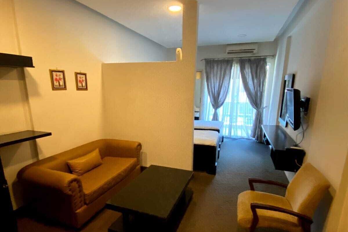 A living room with a sofa, a coffee table, and a chair. There is a TV mounted on the wall and a window with curtains.