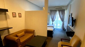 A living room with a sofa, a coffee table, and a chair. There is a TV mounted on the wall and a window with curtains. - Dreams Suites (Beirut)