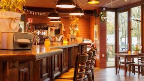 Un espace bar doté d’un comptoir en bois, de plusieurs luminaires suspendus et d’un coin salon avec des chaises et des tables.