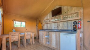Une cuisine compacte dotée de meubles en bois, d’un petit réfrigérateur et d’un téléviseur à écran plat fixé au mur.