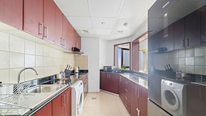 A modern kitchen with stainless steel appliances, a washing machine, and a sink. - WelHome - Stunning High-Rise with Canal View Near MarinaMall (Dubai)