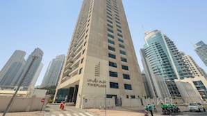 A high-rise building with multiple floors, a prominent entrance, and a clear sky. - WelHome - Stunning High-Rise with Canal View Near MarinaMall (Dubai)