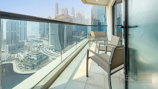 A balcony with a view of a cityscape, including high-rise buildings and a marina. - WelHome - Stunning High-Rise with Canal View Near MarinaMall (Dubai)