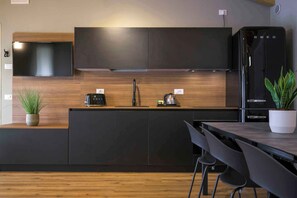 Moderni keittiö, jossa on tummat kaapit, puinen työtaso, sisäänrakennettu liesi, musta jääkaappi ja ruokailutila tuoleineen.