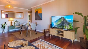 A modern living room with a flat-screen TV, a dining area with a table and chairs, a sofa, and a large painting on the wall. - GuestReady - Idyllic vacation with stunning views (Caniço)