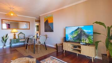 Ein modernes Wohnzimmer mit Flachbildfernseher, einem Essbereich mit Tisch und Stühlen, einer Couch und einem großen Gemälde an der Wand.