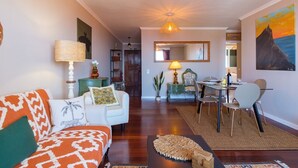 A living room with a sofa, a dining table with chairs, a lamp, and a painting on the wall. - GuestReady - Idyllic vacation with stunning views (Caniço)