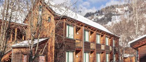 Un edificio de madera de varios pisos con balcones, rodeado de árboles nevados y montañas al fondo.