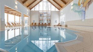 Ein Innenpool mit Holzbalken, großen Glasfenstern und Liegestühlen.