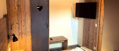 A bedroom with a wooden wardrobe, a bed with towels, a bedside table, and a mounted TV.