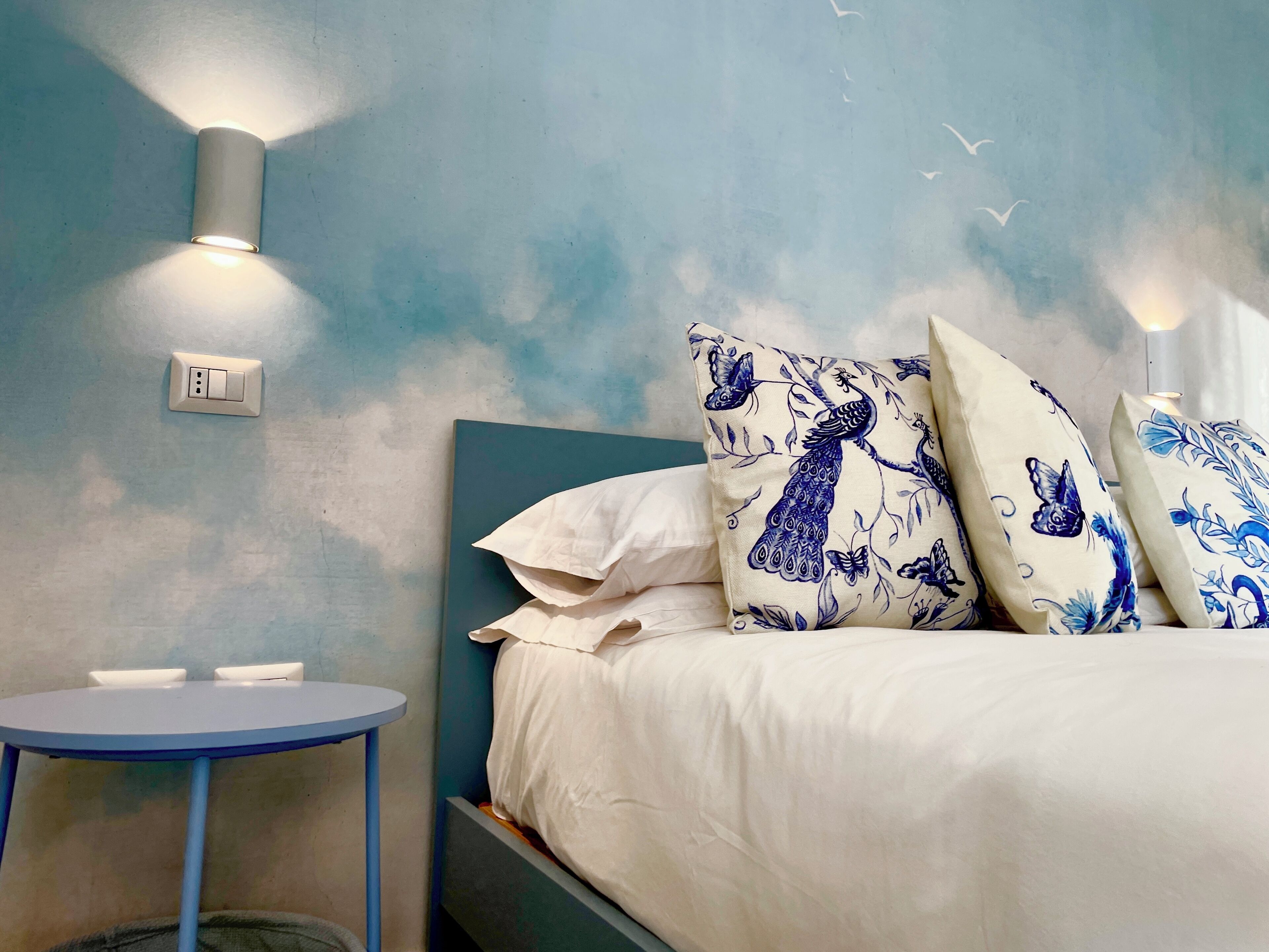 A bedroom with a bed, pillows, a bedside table, and wall-mounted lights.