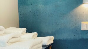 A bathroom with a dark blue wall, a wooden stool with towels, and a round trash bin. - Your home in Rome

4 Rooms & 4 Elements 

Spacious penthouse for 12 guests
 (Roma)