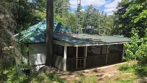 A small cabin with a green roof, surrounded by dense forest.