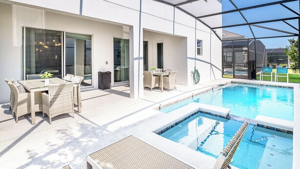 A modern outdoor pool area with a glass-enclosed patio, wicker furniture, and a clear view of the pool. - UpstaySleeps26PrivatePoolHotTubCinemaG (Kissimmee)